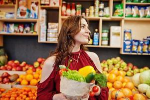 garota de vermelho segurando diferentes vegetais na loja de frutas. foto