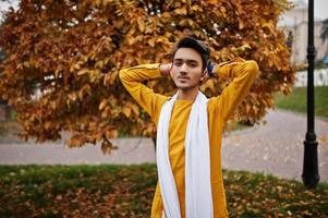 homem elegante indiano em roupas tradicionais amarelas com lenço branco posou ao ar livre contra folhas de outono. foto