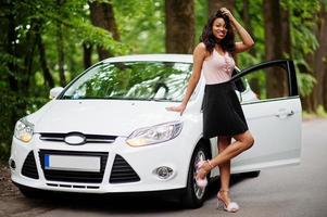 mulher afro-americana posou contra carro branco na estrada florestal. foto