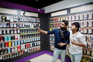 dois índios mans comprador de cliente no celular fazendo selfie por vara monopé. conceito de povos e tecnologias do sul da Ásia. loja de celulares. foto