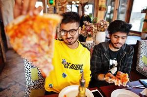 caras amigos asiáticos comendo pizza durante a festa na pizzaria. índios felizes se divertindo juntos, comendo comida italiana e sentados no sofá. foto