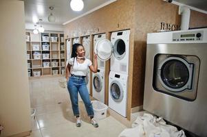 alegre mulher afro-americana perto de máquina de lavar roupa na lavanderia self-service.