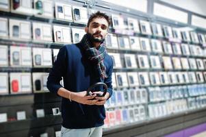 comprador de cliente homem de barba indiana na loja de telefonia móvel com fones de ouvido sem fio. conceito de povos e tecnologias do sul da Ásia. loja de celulares. foto
