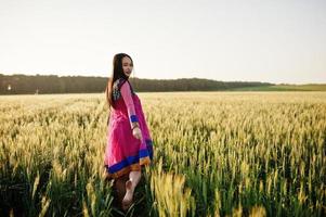 tenra garota indiana em saree, com lábios violeta compõem posou no campo no pôr do sol. modelo elegante da índia. foto