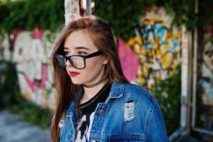 garota elegante hipster casual em jeans e óculos contra a grande parede de graffiti. foto