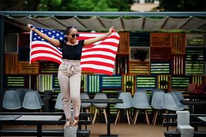 mulher afro-americana elegante em óculos de sol posou ao ar livre com bandeira dos eua. foto