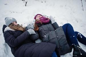 duas amigas engraçadas se divertindo no dia de inverno nevado perto de árvores cobertas de neve. foto