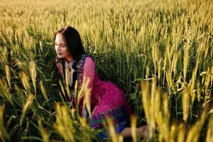 tenra garota indiana em saree, com lábios violeta compõem posou no campo no pôr do sol. modelo elegante da índia. foto