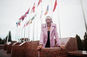 jovem elegante linda afro-americana na rua, vestindo óculos e casaco de roupa de moda, contra bandeiras de diferentes países do mundo. foto