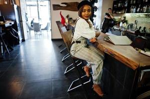 mulher afro-americana de macacão e boina sentada no balcão do bar. foto
