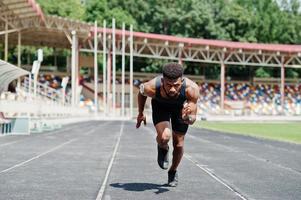 atleta masculino americano africano em roupas esportivas correndo sozinho em uma pista de corrida no estádio. foto