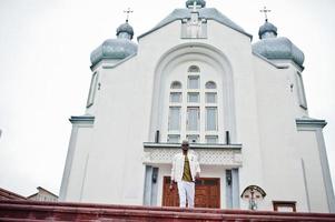 homem afro-americano de chapéu e óculos de sol fica contra a igreja. fé e cristianismo na África. foto