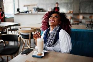 garota encaracolada afro-americana atraente sentado no café com café com leite. foto