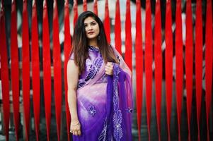 garota hindu indiana no tradicional saree violeta posou na rua contra um fundo vermelho. foto