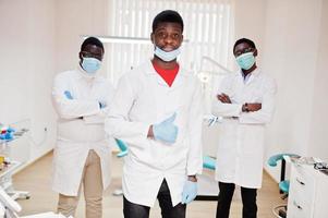 três médicos afro-americanos com braços cruzados na clínica odontológica. mostrar o polegar para cima. foto