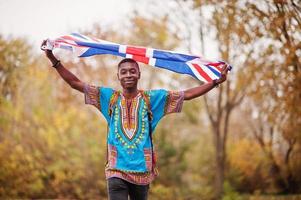 homem africano na camisa tradicional da África no parque outono com bandeira da Grã-Bretanha. foto