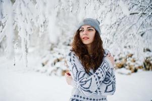 linda garota encaracolada na camisola e chapéus no parque florestal nevado no inverno. foto