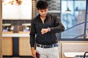 homem indiano elegante posou no café de fast food com o celular na mão e olhando para os relógios. foto
