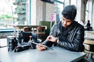 fotógrafo de jovem asiático inteligente trabalhando com tablet durante sentado no café e olhando para seus relógios. foto