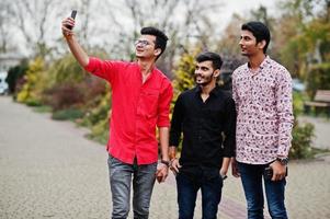 três caras indianos estudantes amigos andando na rua e faz selfie no celular. foto