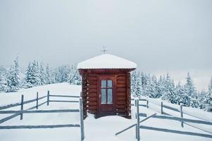 capela de madeira pequena igreja em pinheiros cobertos de neve na montanha chomiak. belas paisagens de inverno das montanhas dos cárpatos, ucrânia. natureza geada. foto