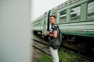 retrato de estilo de vida de homem bonito com mochila posando na estação de trem. foto