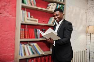 forte e poderoso homem afro-americano de terno preto leu livro contra prateleiras em livros grátis anti café. foto