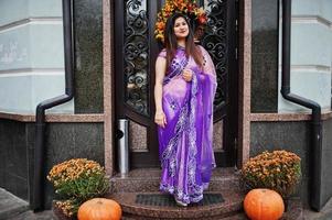 garota hindu indiana no tradicional saree violeta posou na rua contra a porta do restaurante com clima de outono e abóboras. foto