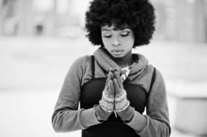 mulher afro-americana de cabelo encaracolado com luvas, mãos juntas como rezar, posou em dia de inverno. foto