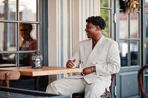 homem afro elegante em terno bege old school sentado no café. elegante jovem homem africano na jaqueta casual no torso nu. foto