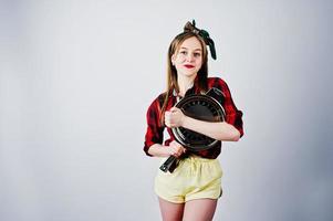 jovem dona de casa engraçada na camisa quadriculada e short amarelo pin up estilo com frigideira isolada no fundo branco. foto