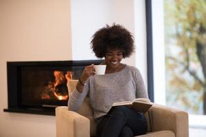 mulher negra lendo livro em frente a lareira foto