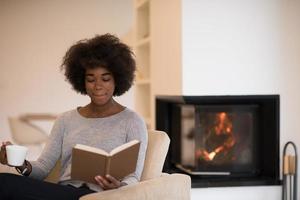 mulher negra lendo livro em frente a lareira foto