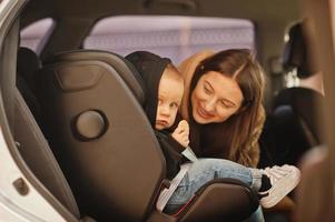 jovem mãe e filho no carro. assento de bebê na cadeira. conceito de condução de segurança. foto