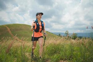 trilha ativa de mulheres jovens atravessando um prado em uma trilha gramada no alto das montanhas à tarde com vara de trekking foto