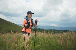 trilha ativa de mulheres jovens atravessando um prado em uma trilha gramada no alto das montanhas à tarde com vara de trekking foto