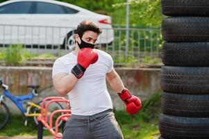 retrato esportivo homem boxer árabe em máscara facial médica preta boxe ao ar livre durante a quarentena de coronavírus. foto