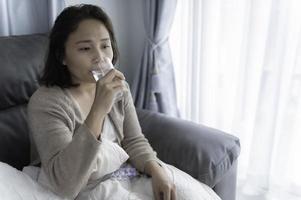 mulher asiática doente sente-se no sofá ficar em casa, a mulher se sentiu mal, queria deitar e descansar, febre alta