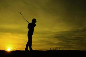 silhueta golfista asiático jogando golfe durante o belo pôr do sol foto