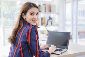 mulher confiante asiática está descansando a mão no teclado do laptop e vira o rosto sorrindo em uma sala de trabalho em casa. foto