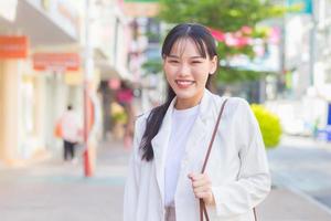 mulher trabalhadora asiática de negócios jovem confiante que veste uma camisa branca e uma bolsa de ombro sorri alegremente enquanto ela está caminhando para trabalhar no escritório na cidade. foto