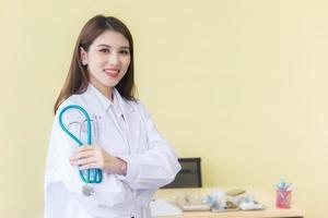 médico jovem bela mulher asiática em pé com os braços cruzados feliz e sorriso no hospital. vestindo uma túnica branca e estetoscópio foto