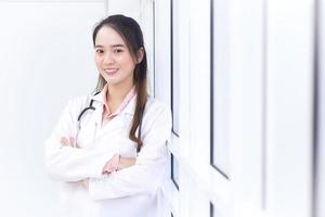 médica asiática com cabelos longos pretos usa um jaleco branco e estetoscópio.