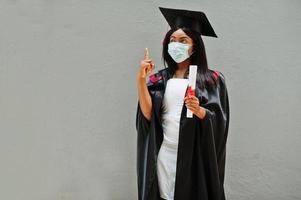 jovem estudante de pós-graduação afro-americana usa uma máscara protetora contra coronavírus. conceito de cerimônia de formatura, quarentena. foto