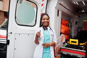 paramédico feminino americano africano em frente ao carro da ambulância. foto