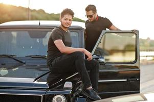 dois irmãos asiáticos vestem todo preto posando perto do carro suv. foto