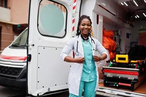 paramédico feminino americano africano em frente ao carro da ambulância. foto