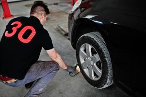 tema de reparação e manutenção de automóveis. mecânico de uniforme trabalhando em auto serviço, verificando pneus. foto