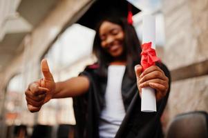 jovem estudante afro-americana com diploma posa ao ar livre. foto