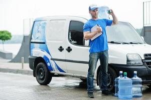 entregador com prancheta na van de carga frontal entregando garrafas de água. foto